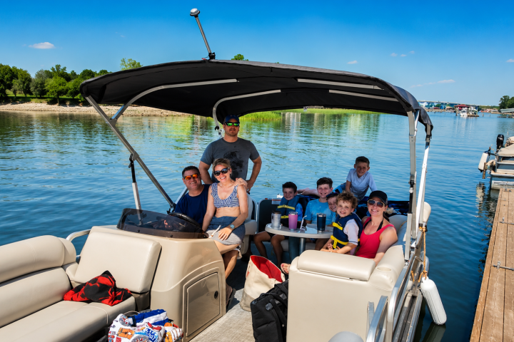 Group of people smiling on a pontoon boat on a sunny day.