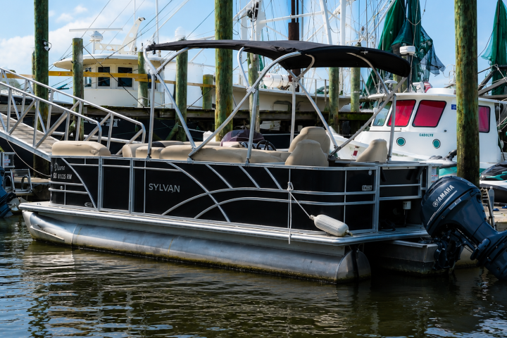 Pontoon boat docked beside sailboats in a marina.