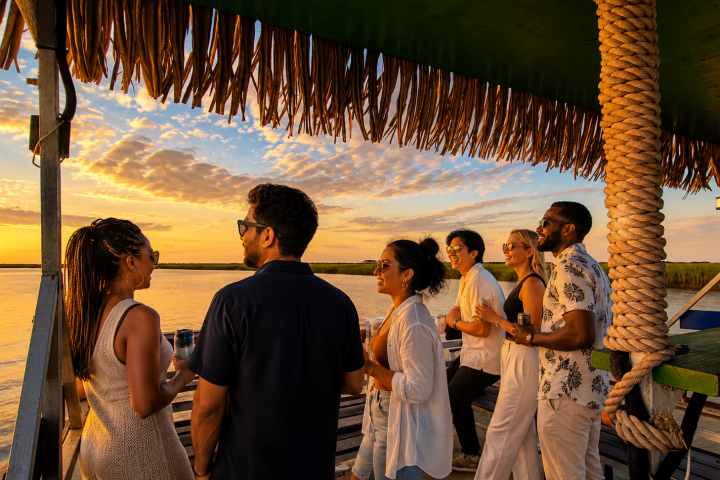 Group of people enjoying a sunset on a boat with a thatched roof.