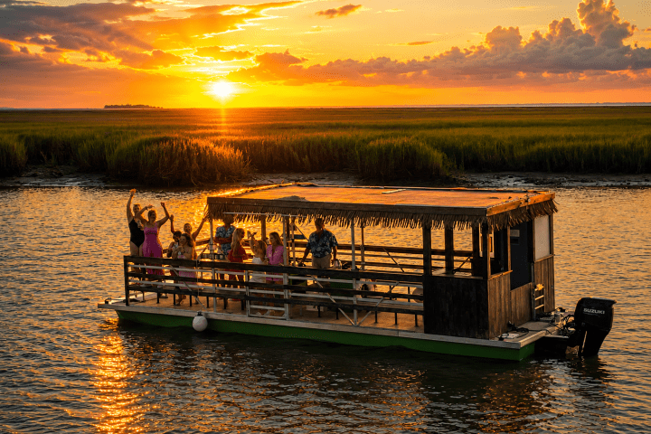 People on a pontoon boat at sunset with vibrant sky and lush greenery.