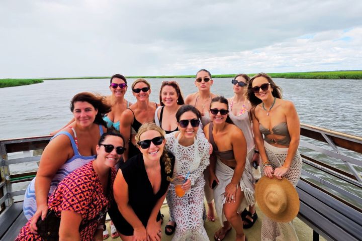 Group of women posing on a boat with a river and grassy banks in the background.