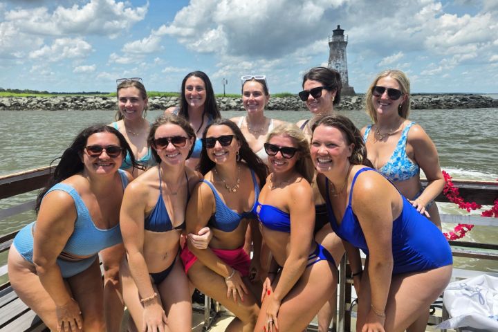 Group of women in swimsuits posing on a dock with a lighthouse in the background.