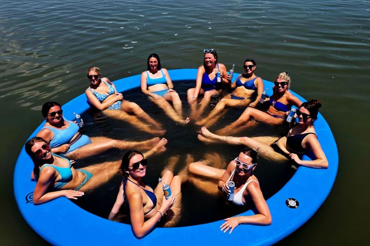 Group of women in swimsuits relaxing on a floating circular raft in the water.