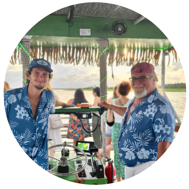 Two men in blue floral shirts on a boat with people in the background.