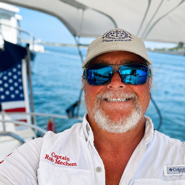 Smiling man in sunglasses and cap on a boat, ocean background.